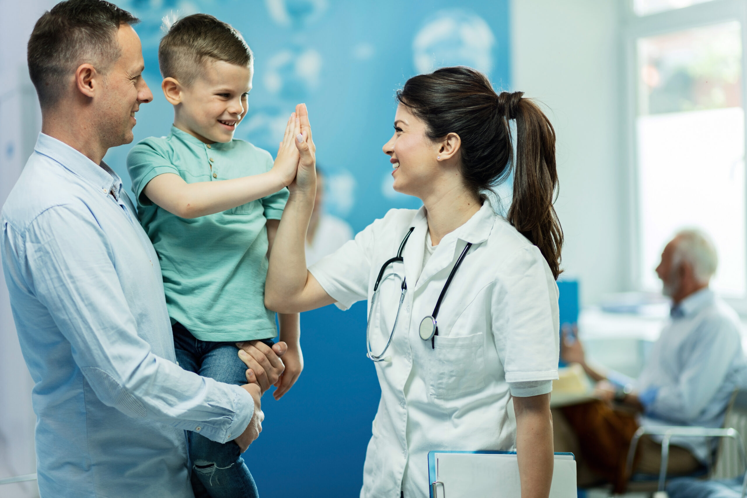 Happy female doctor giving high fie to a little boy who came with father at hospital.