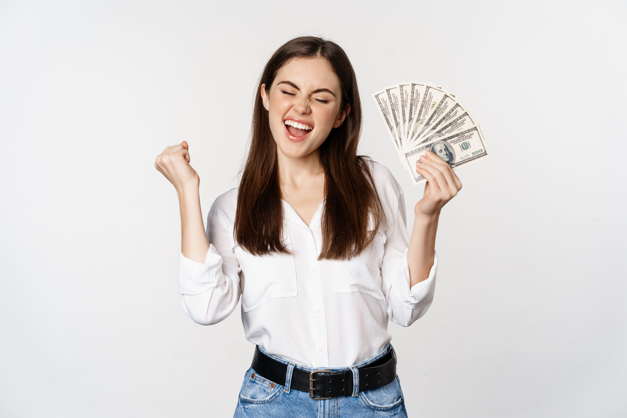 Joyful woman dancing with money, smiling pleased, winning prize, standing over white background.